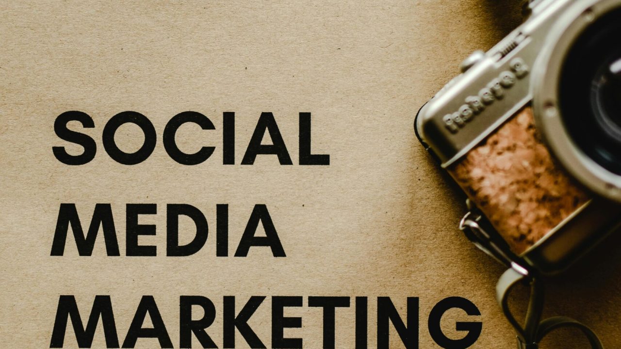 Close-up of a vintage camera next to a social media marketing concept text on a brown background.